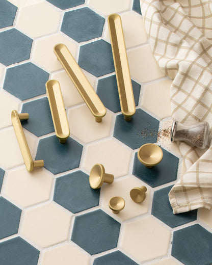 Overhead view of Rhone Knob in cast brass, with matching brass pulls and knobs on blue and cream hexagonal tiles