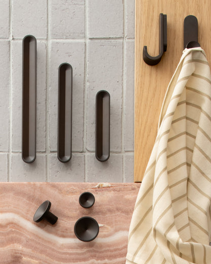 Top view of Rhone Knob showcasing minimalist textured forms with hardware on tile, wood, and stone surfaces
