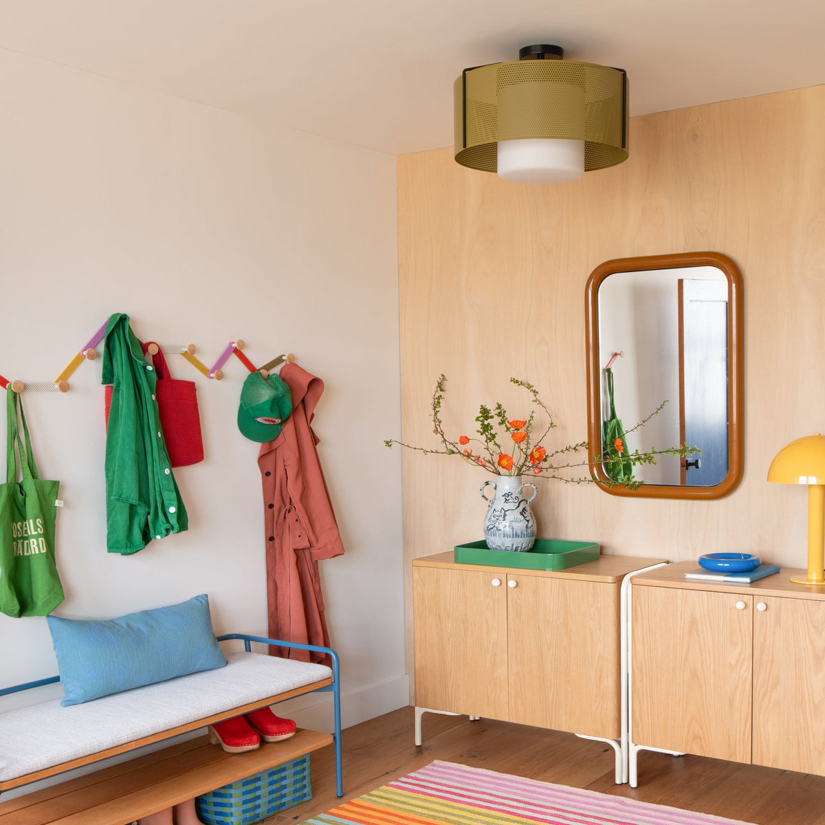 Colorful Tula hooks holding coats, bags, and hats on a wall in a bright room