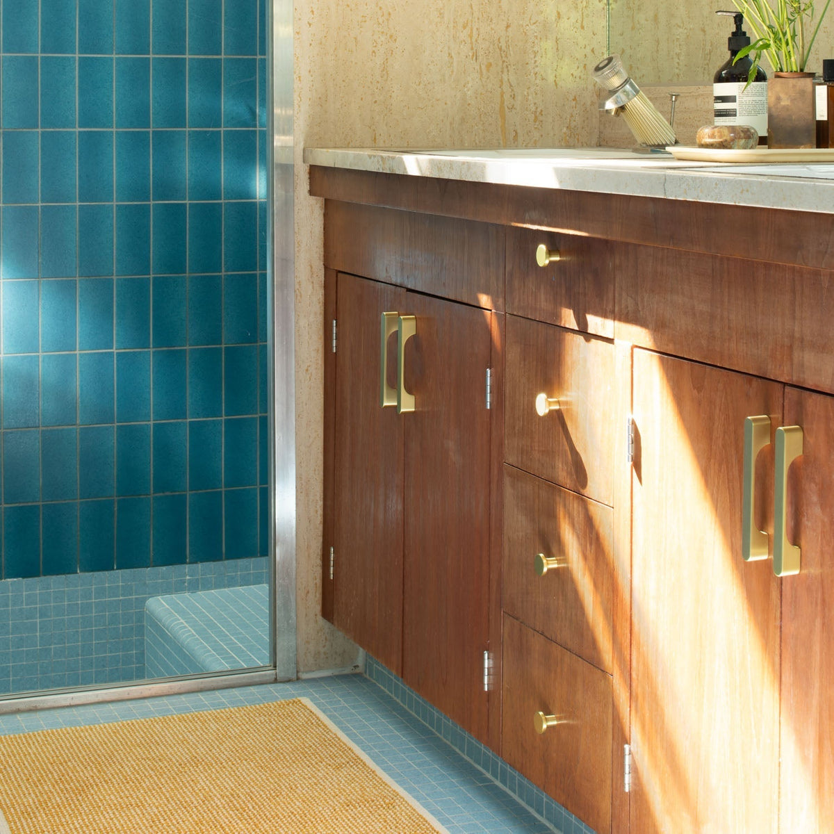 Solid-brass cabinet knobs installed on a wood vanity beside a blue-tiled shower