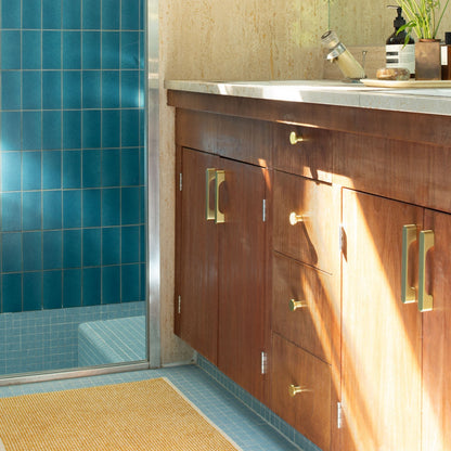Solid-brass cabinet knobs installed on a wood vanity beside a blue-tiled shower