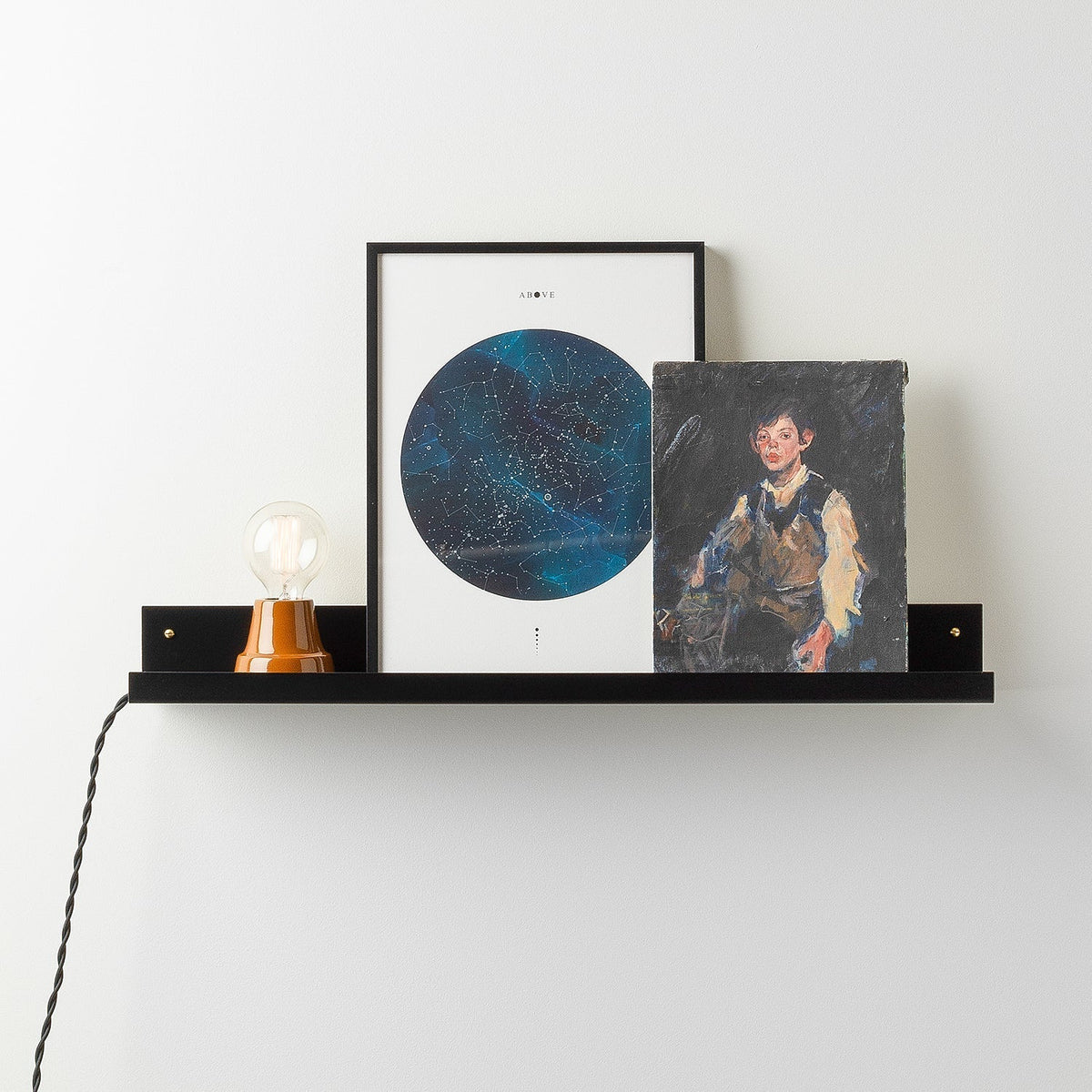 Front view of the black satin Brake Angle Picture Ledge showcasing framed art with a white wall background