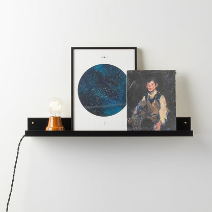 Front view of the black satin Brake Angle Picture Ledge showcasing framed art with a white wall background