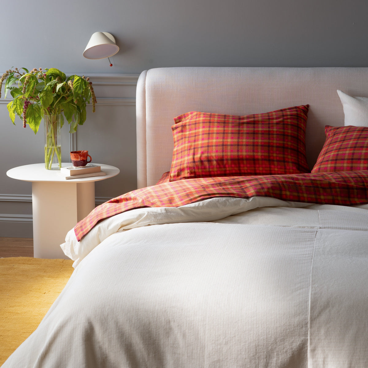 Bedroom with a white bed, red plaid bedding, potted plant, and round side table