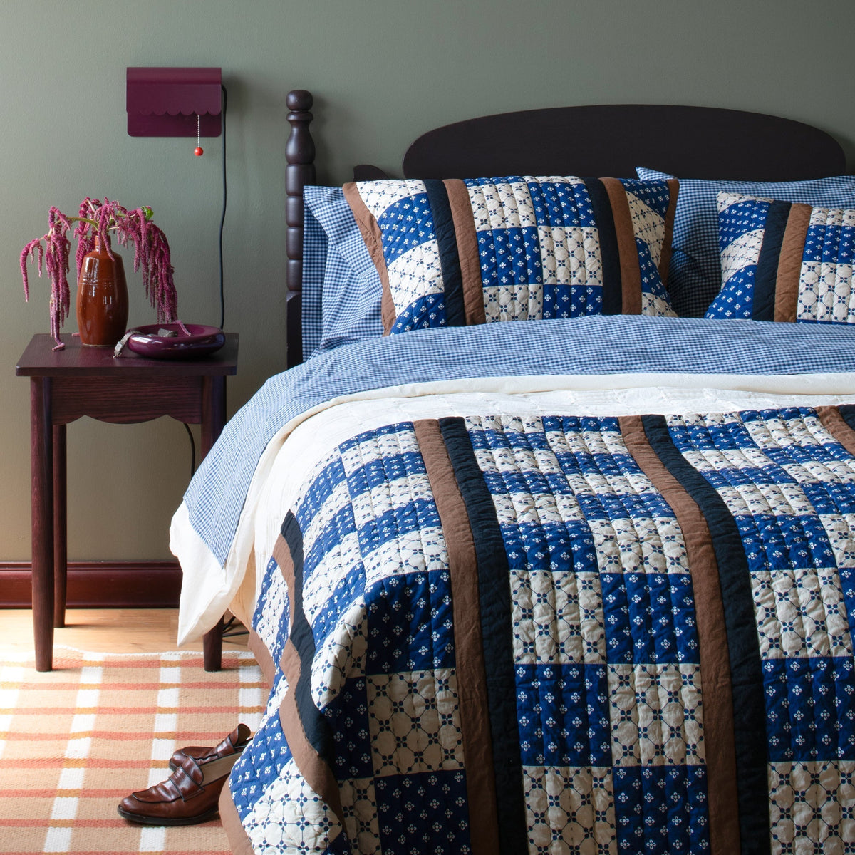 Blue gingham pillowcases arranged on a bed with a patterned quilt and bedside table