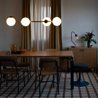 Front view of Aurora Linear showcasing four globe lights on a brass bar with a dining room background