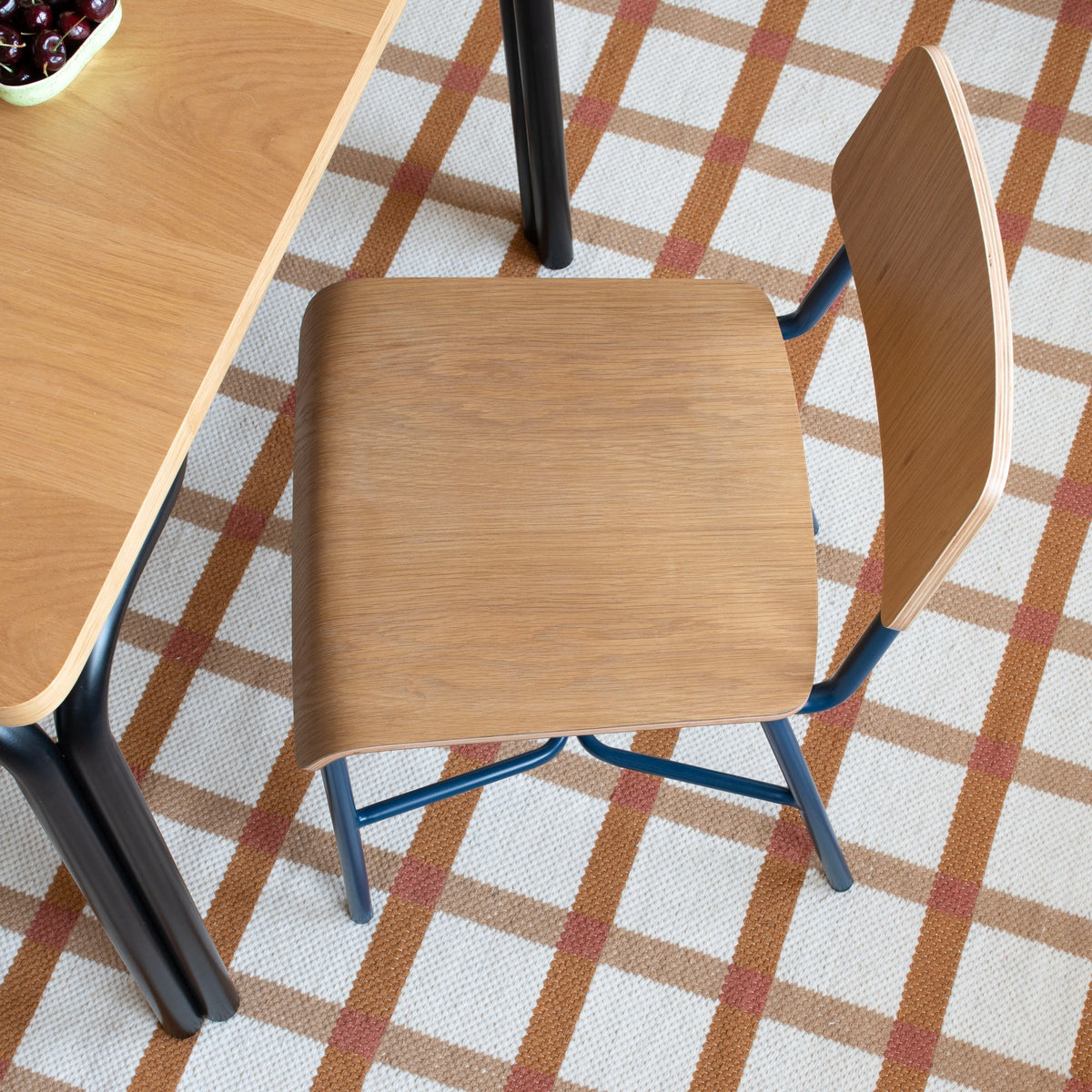 Angled view of Plaid Wool Rug showcasing its cream, brown, and rust plaid pattern beneath a table and chairs