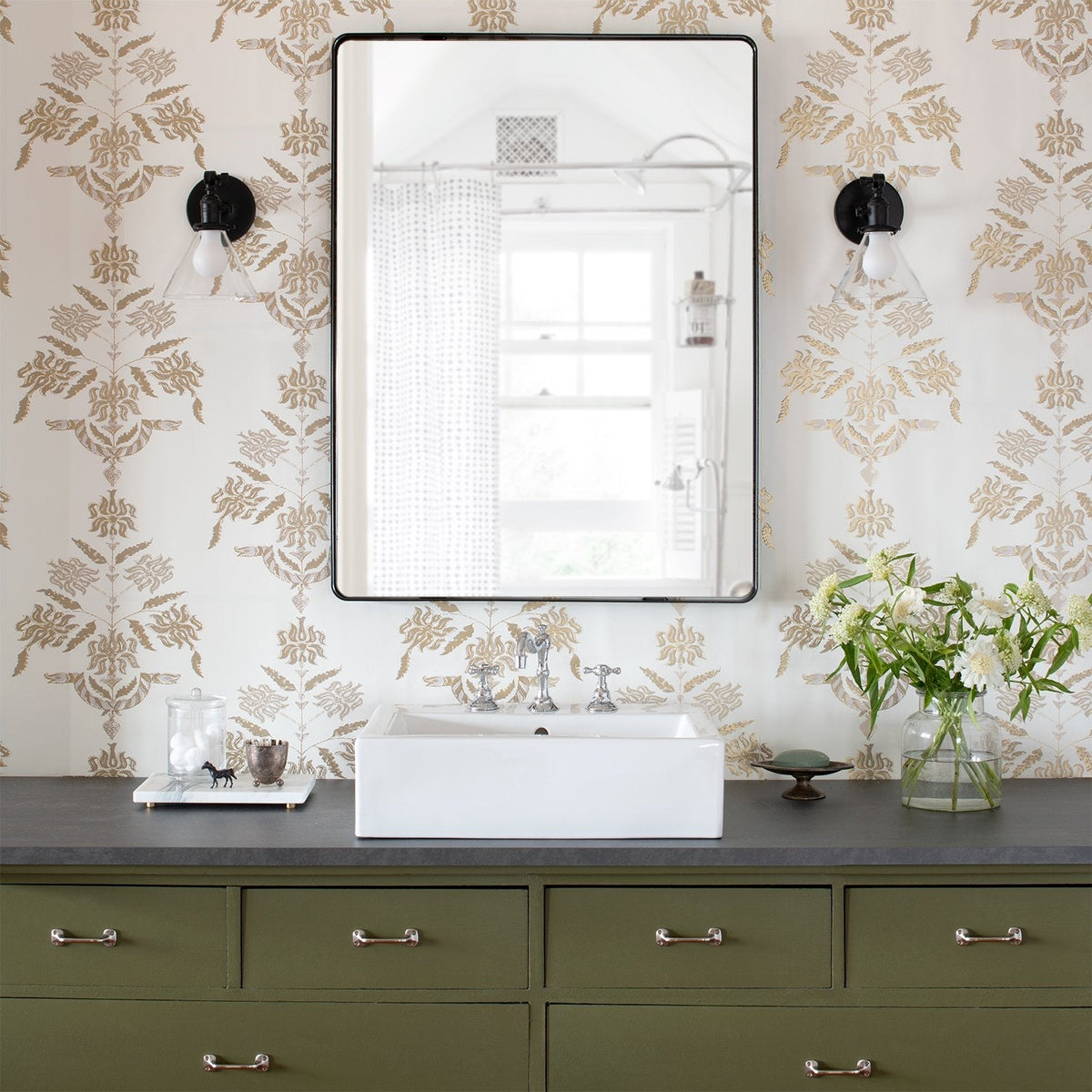 Leo Mirror mounted above a bathroom sink with patterned wallpaper, sconces, and flowers