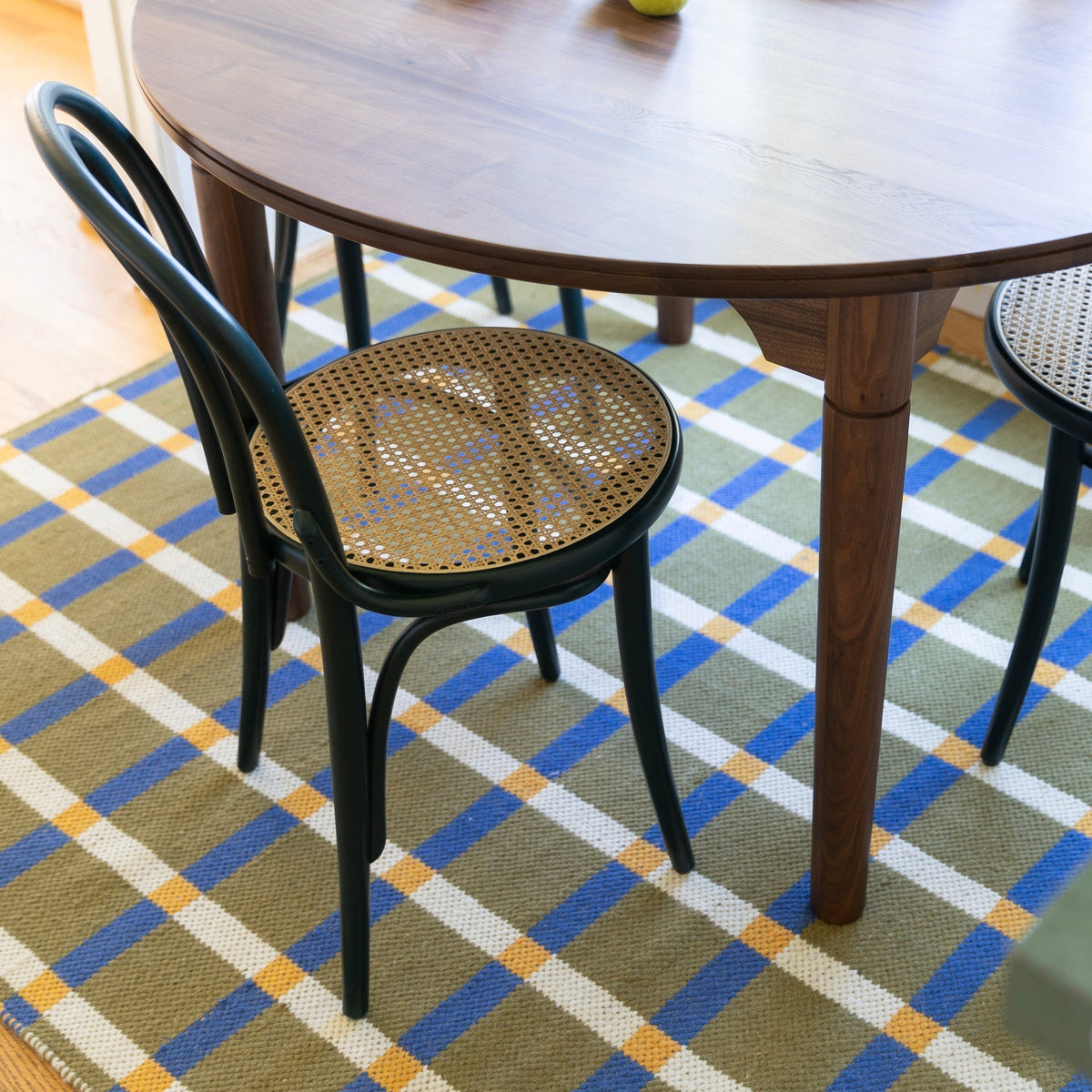 Olive plaid wool rug anchors a dining area beneath a round wood table and black chairs