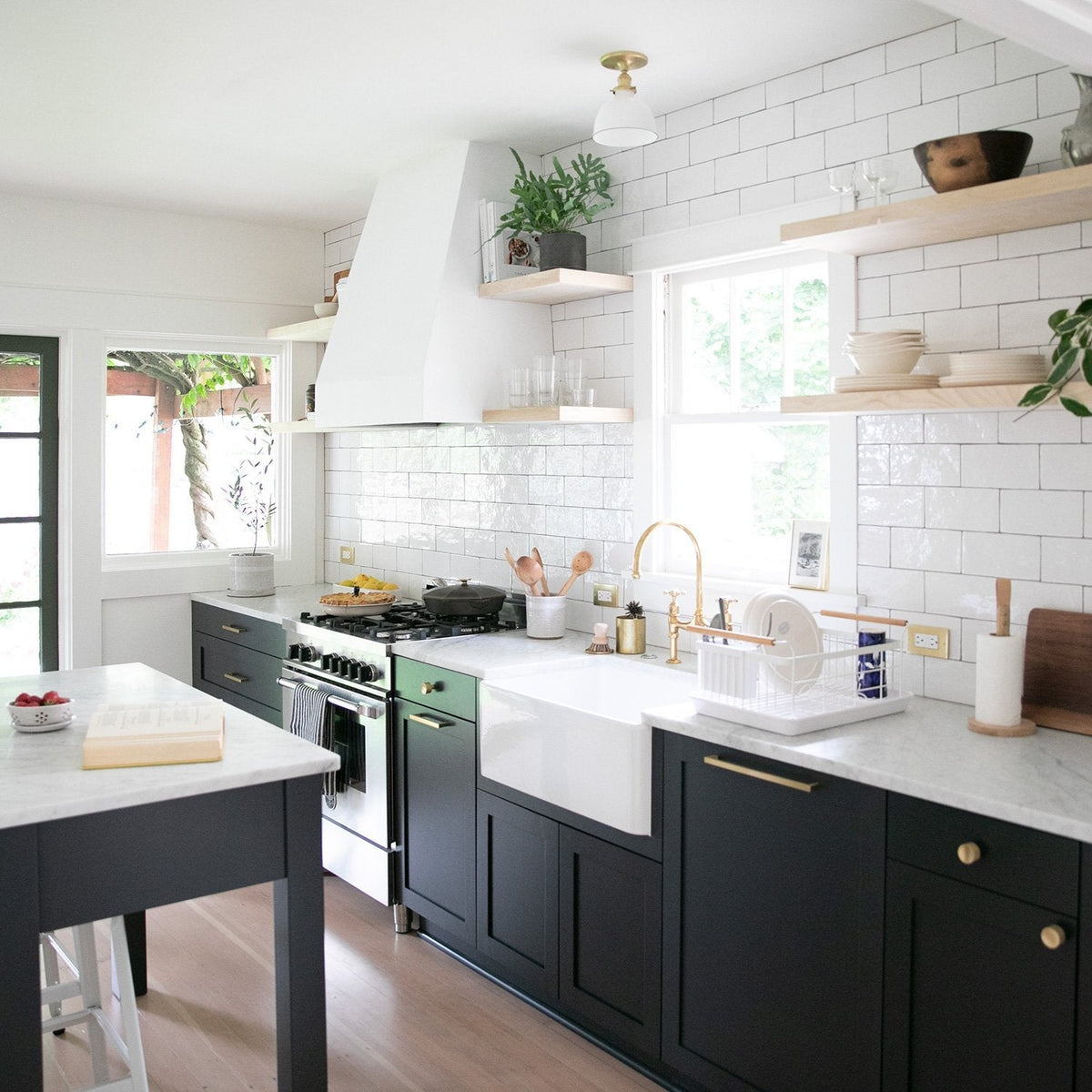 Kitchen with Edgecliff appliance pulls on dark cabinetry, white tile backsplash, open shelves, and a farmhouse sink