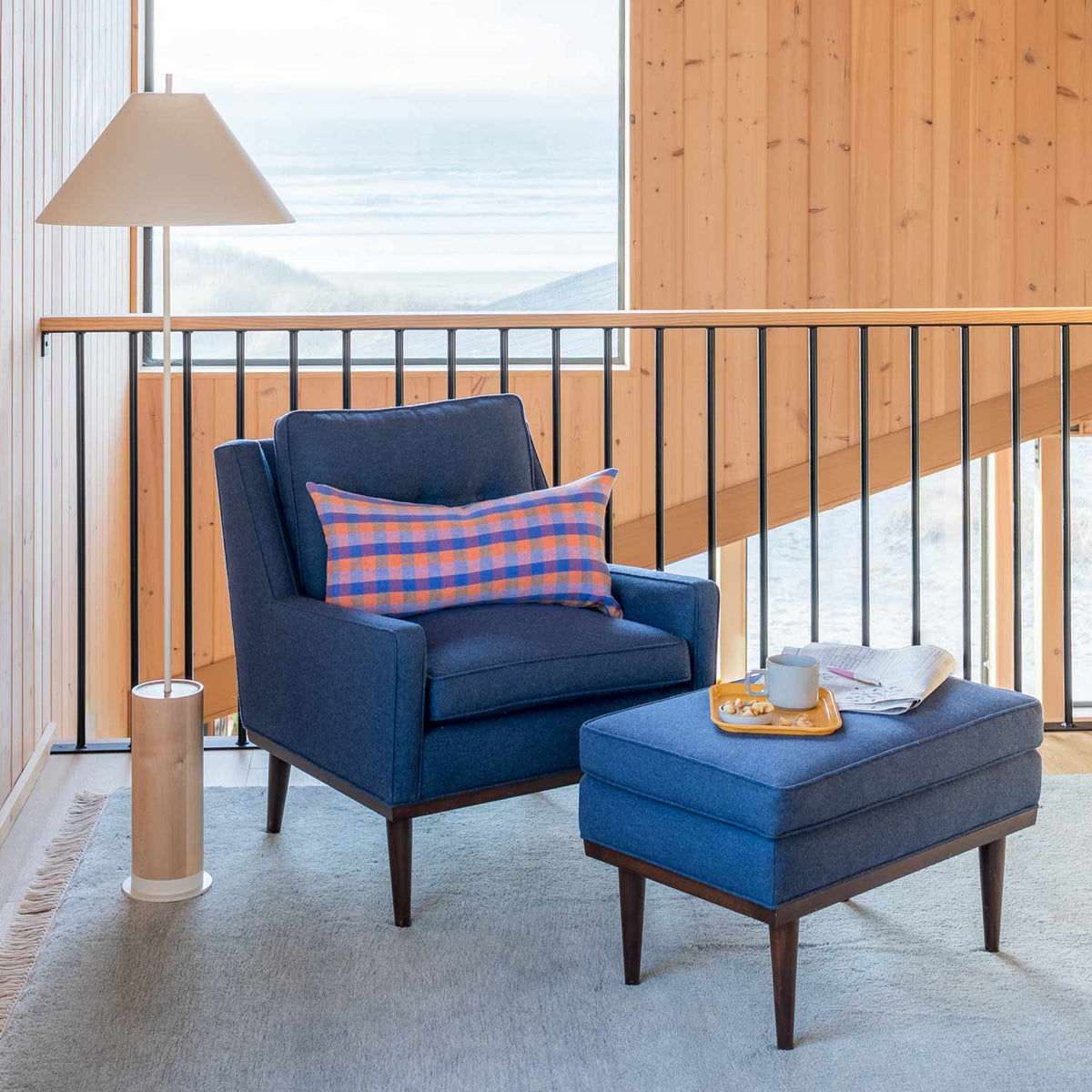 Fog wool rug grounds a navy armchair and ottoman in a wood-paneled room