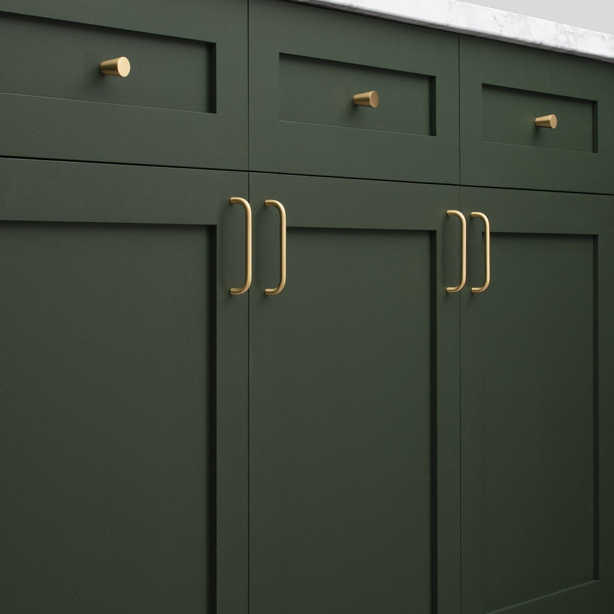 Close-up of Parker Pull cabinet handles showcasing a brass-colored finish on dark green cabinetry