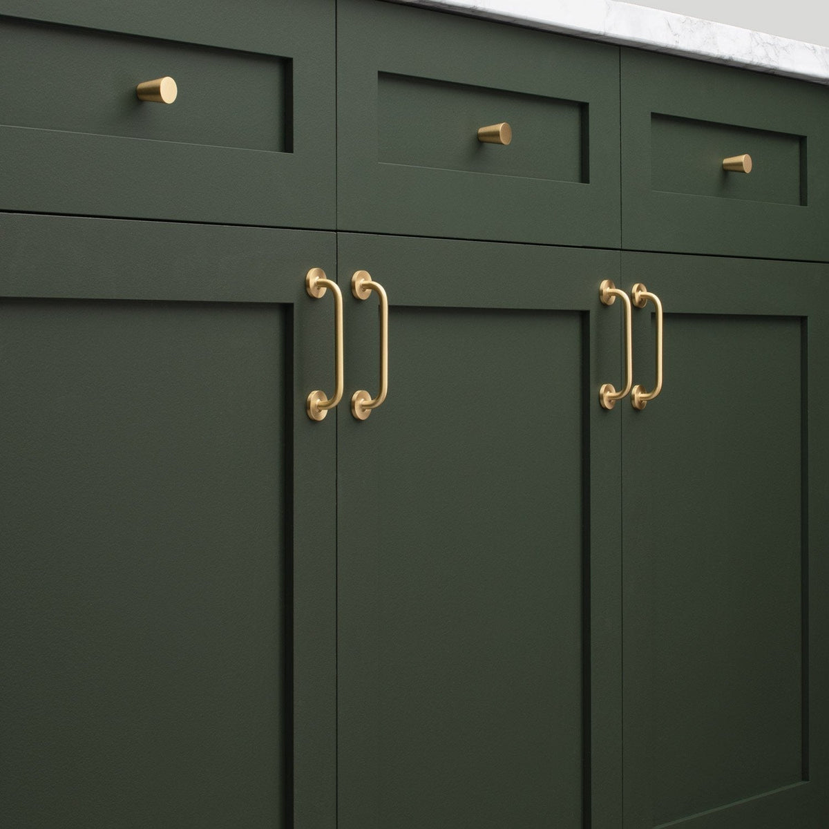 Close-up of Parker Pull showcasing brass hardware on dark green cabinetry