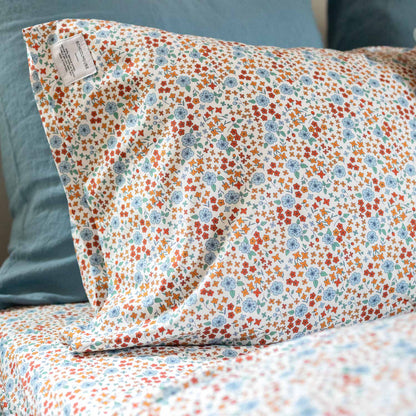 Close-up of Wallowa Floral Percale pillowcase showcasing small orange and blue floral print on white 100% cotton percale with teal pillow background