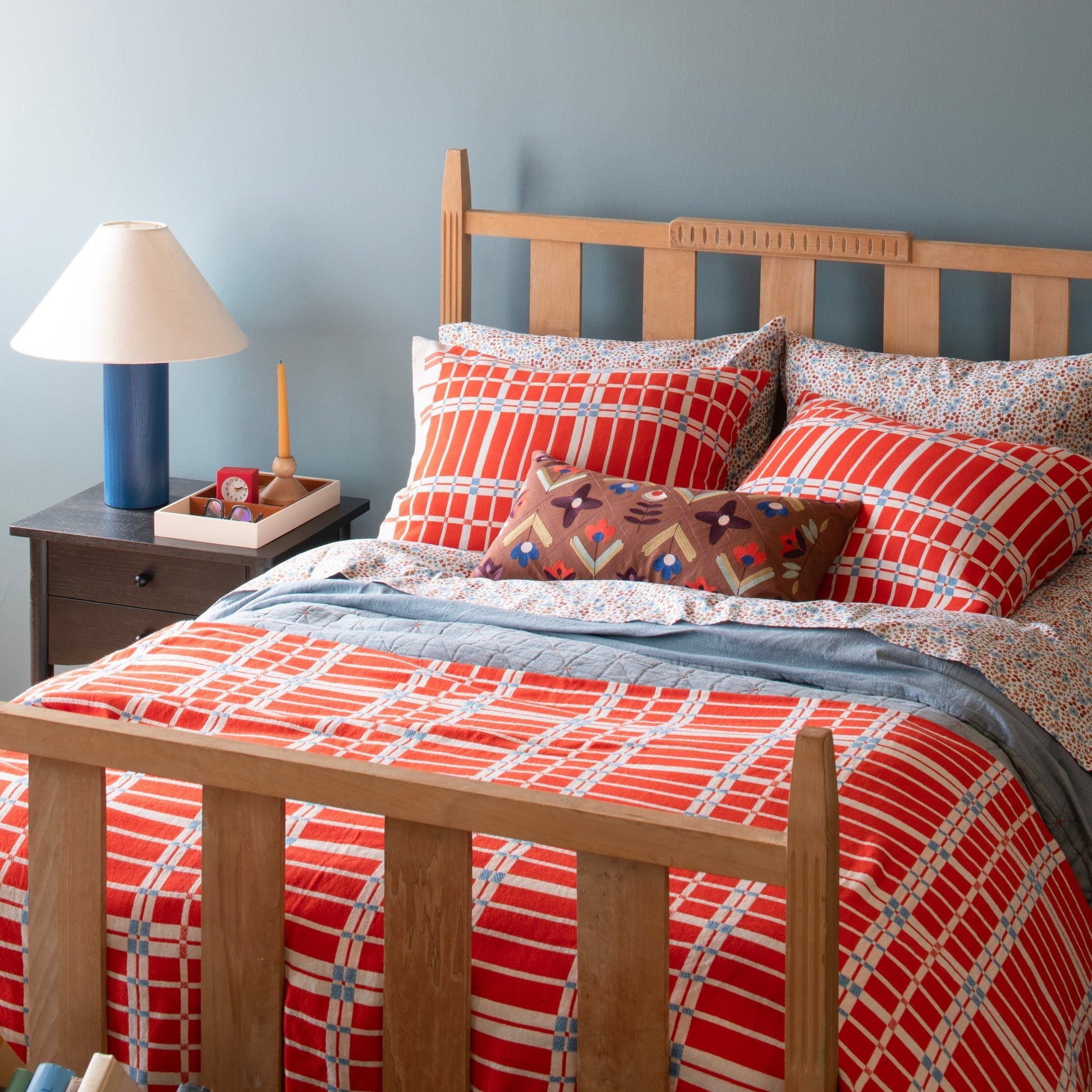Angled view of Wallowa Floral Percale sheet set showcasing chamomile floral pillow shams and cotton percale on a bed with wooden headboard and blue wall