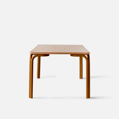 Front view of Forma Dining Table showcasing light oak tabletop and curved rust-colored tubular legs on white background