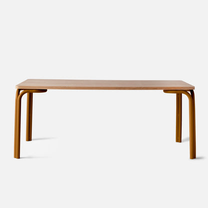 Front view of Forma Dining Table showing light oak tabletop and rounded amber tubular legs on white studio background