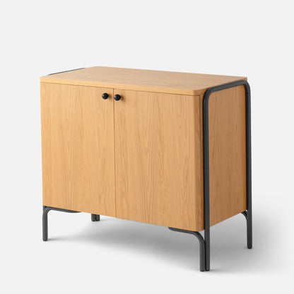 Angled close-up of Forma Cabinet showing oak-veneer doors, black knobs, and powder-coated steel frame on gray background