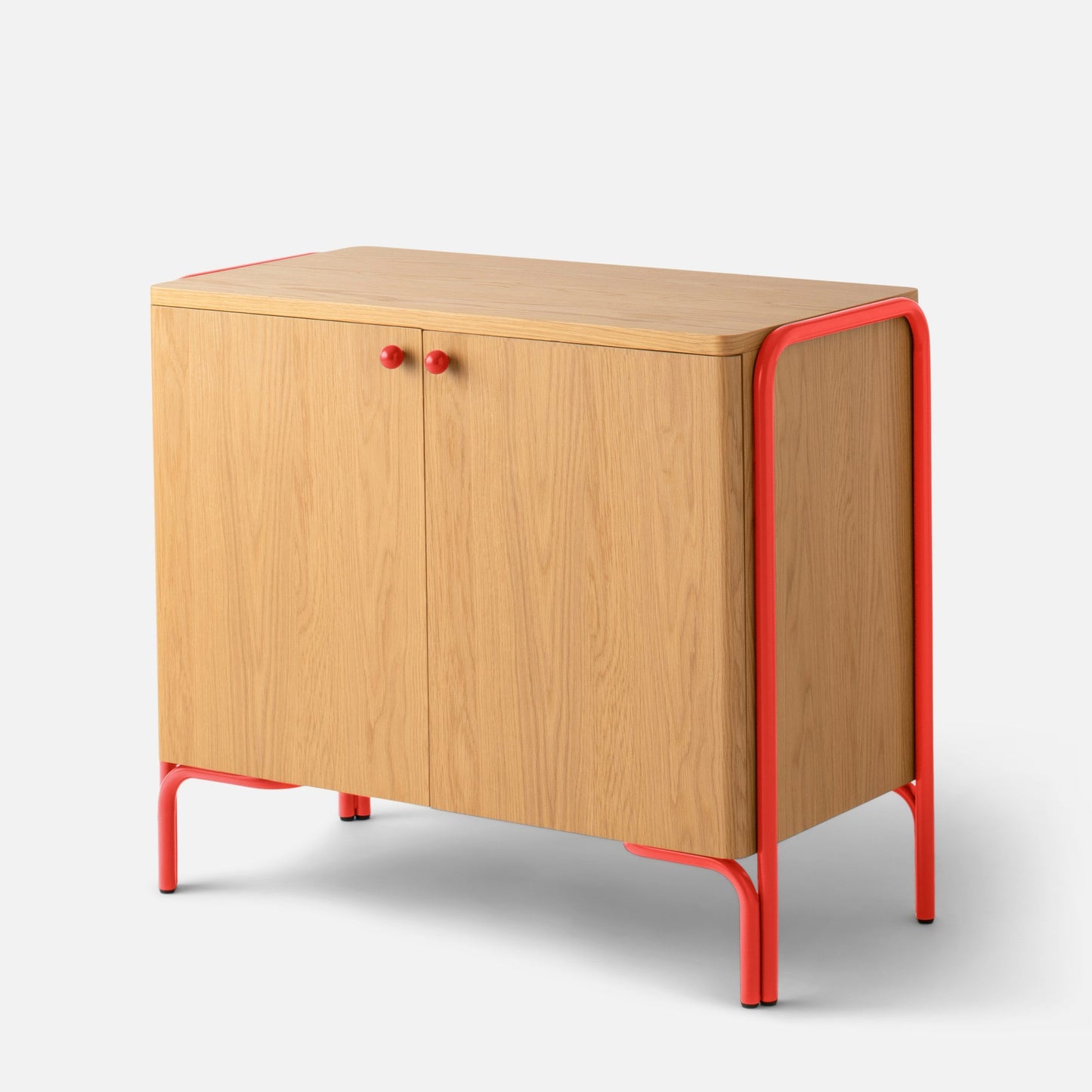 Angled front view of Forma Cabinet showing oak-veneered doors, red powder-coated steel frame and round red knobs on white