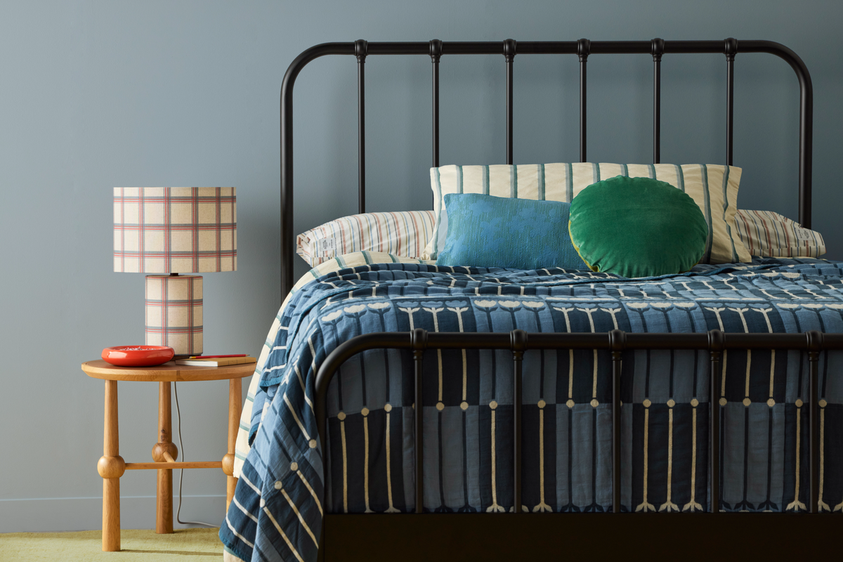Styled bedroom with a black metal bed, patterned blue bedding, colorful pillows, and a plaid table lamp