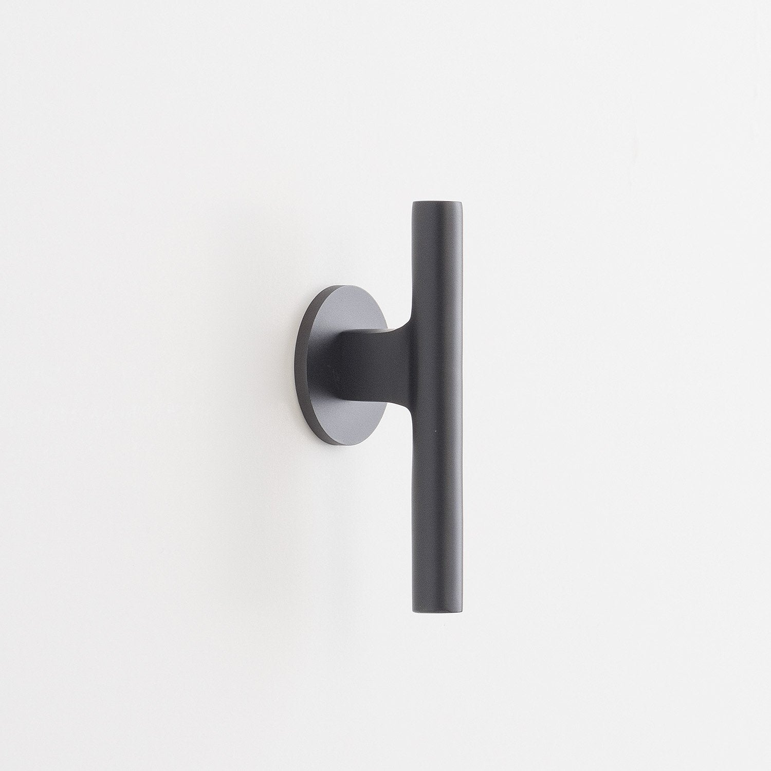 Side view of Galley Pull showing matte black cylindrical bar and round backplate on a white wall