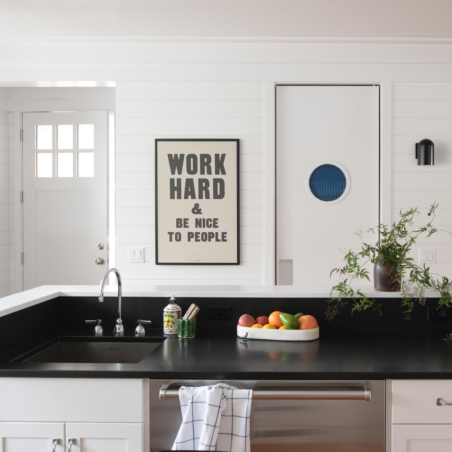 Black Allegheny 4.5-inch wall sconce in a kitchen, mounted on white shiplap next to a framed poster reading WORK HARD & BE NICE TO PEOPLE