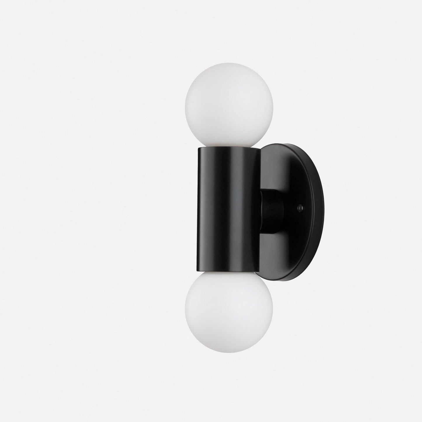 Side view of Cylinder Double Sconce showcasing matte black cylindrical body with two white glass globe bulbs and round wall plate on light gray background