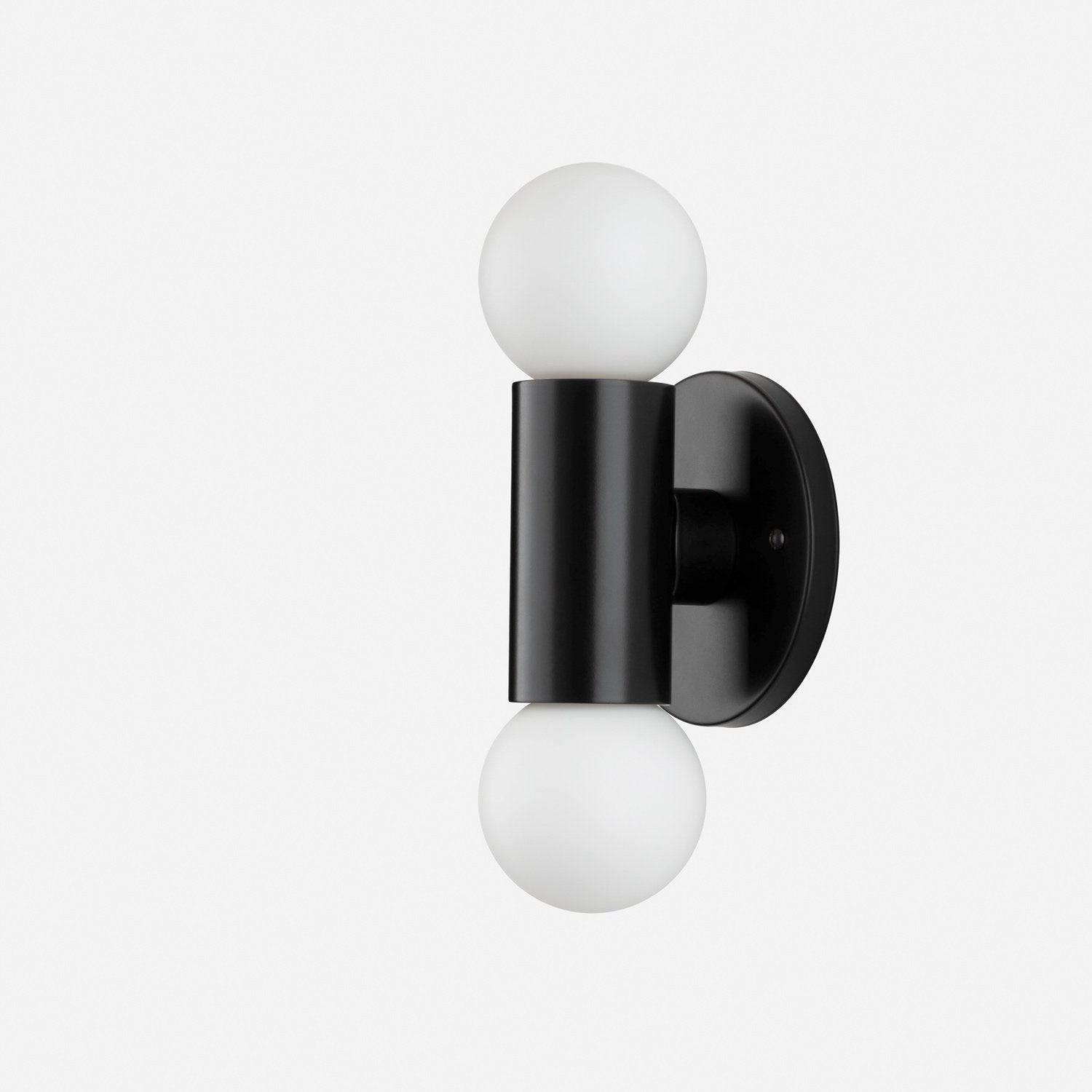 Side view of Cylinder Double Sconce showcasing matte black cylindrical body with two white glass globe bulbs and round wall plate on light gray background