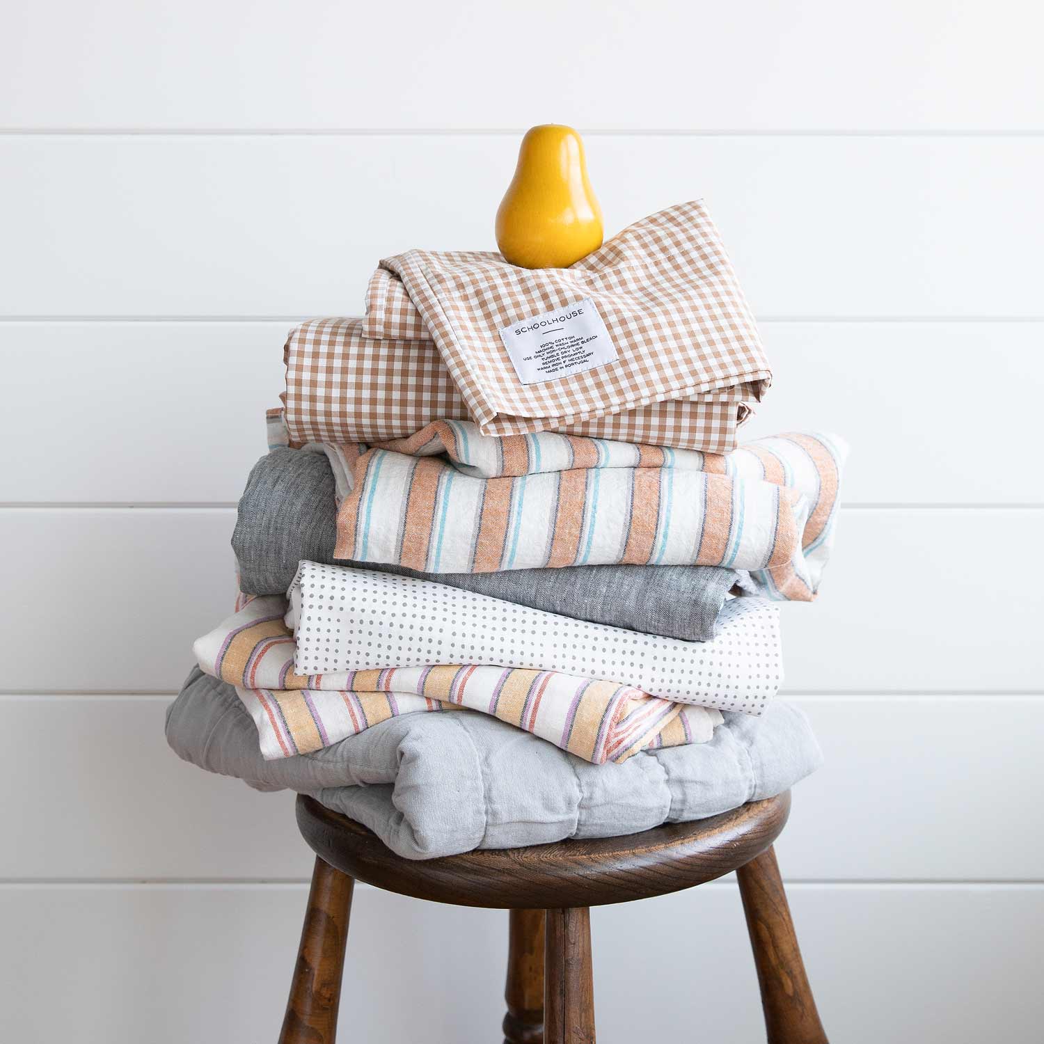 Stacked view of russet gingham pillowcase set (2) showing check pattern and Schoolhouse label on top of folded linens on a wooden stool