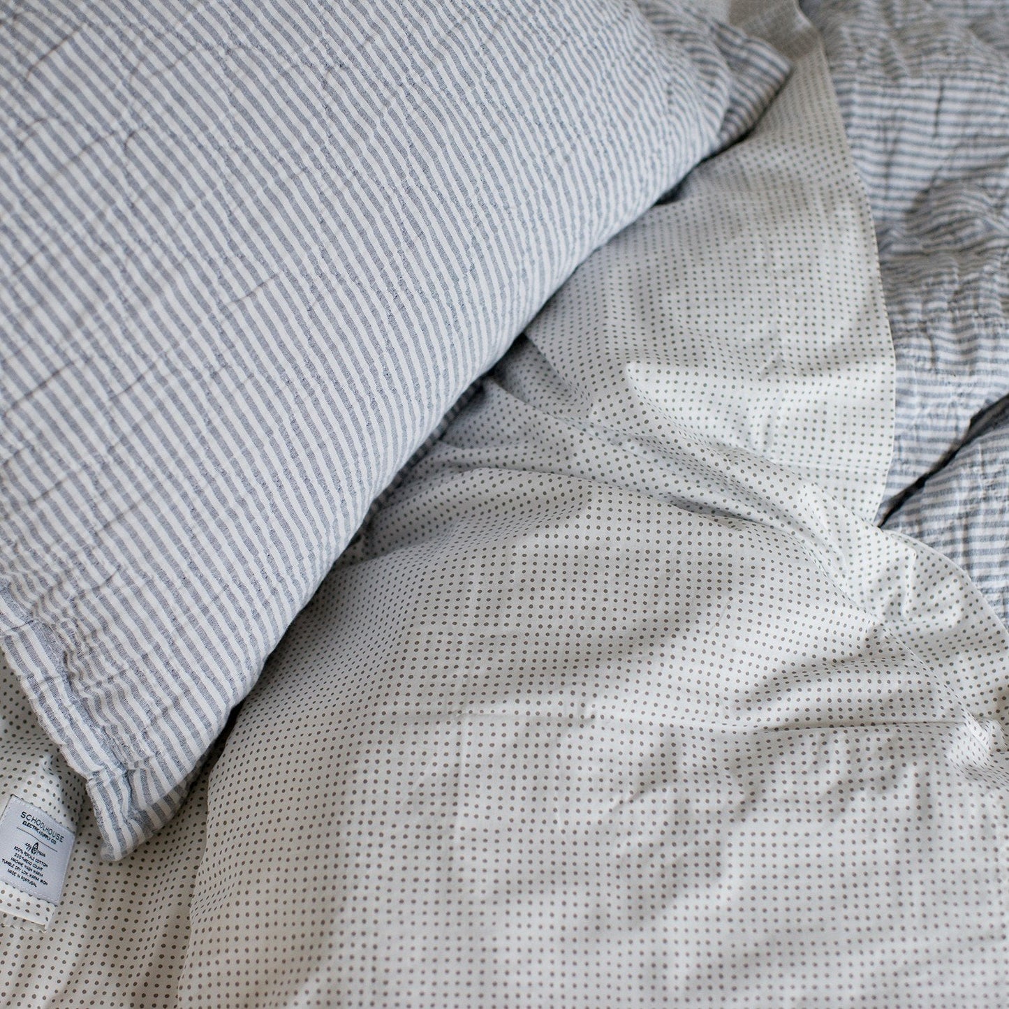 Close-up of Diamond Ticking Quilted Pillow Sham showing ticking stripes and diamond quilting on a dotted white sheet