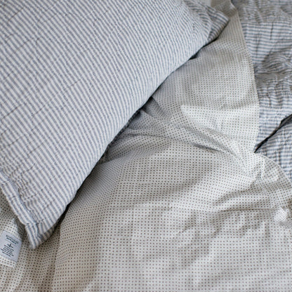 Close-up of Diamond Ticking Quilted Pillow Sham showing ticking stripes and diamond quilting on a dotted white sheet