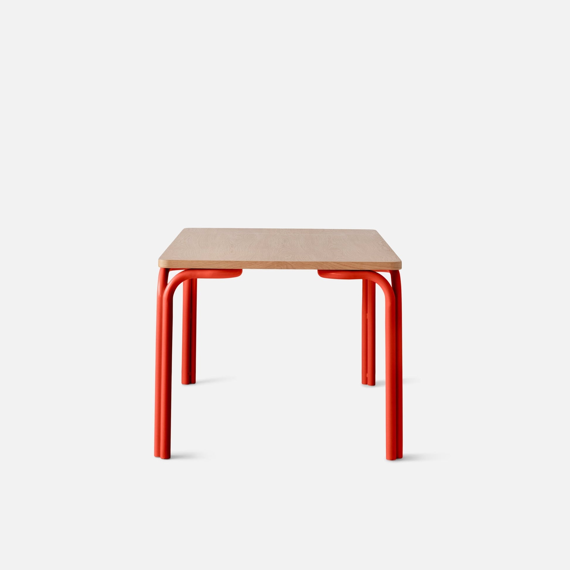 Front view of Forma Dining Table showing light oak rectangular top and red tubular metal legs on white background