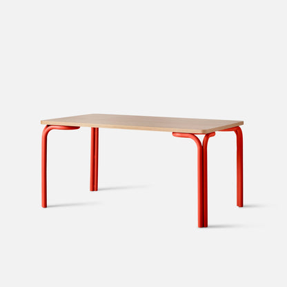 Angled close-up of Forma Dining Table showcasing light oak tabletop and coral-red tubular metal legs on white background