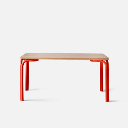 Front view of Forma Dining Table showing light oak top and red tubular metal legs against a white background