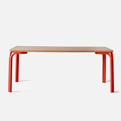 Front view of Forma Dining Table showcasing light oak tabletop and red tubular metal legs on white background
