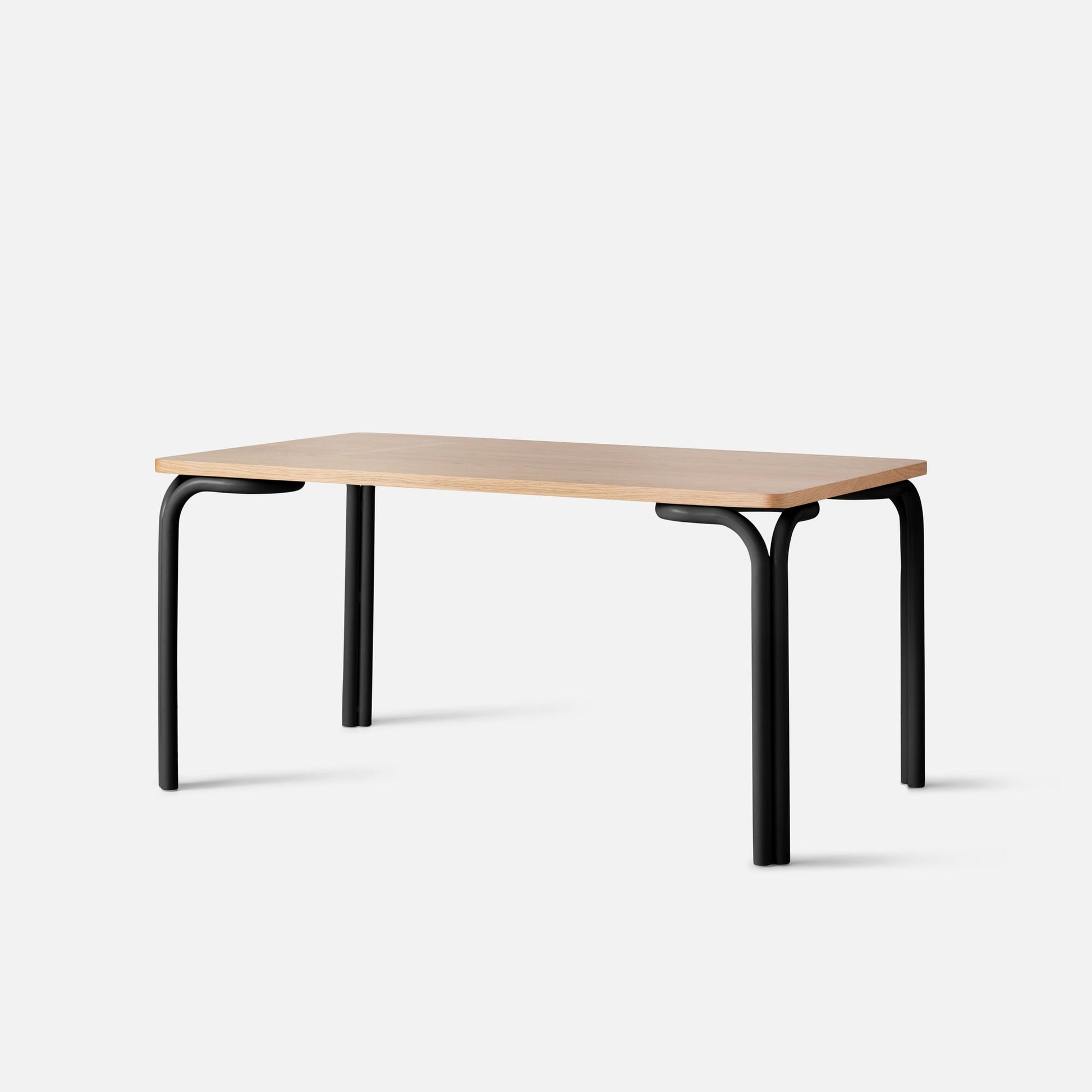 Three-quarter view of Forma Dining Table showing butterscotch satin wood top with rounded edges and curved matte-black tubular legs on a white studio background